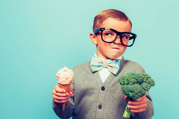 bambini con gli occhiali che tiene in mano un gelato e un broccolo